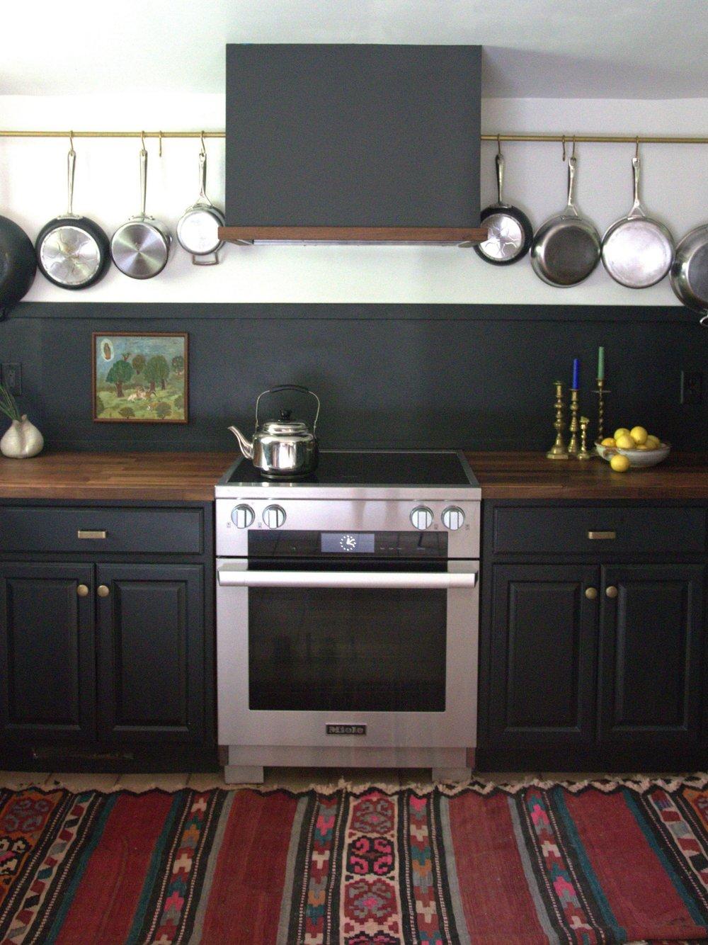 Country Home kitchen designed by Leah Kochaver, with hanging pans, timber counters, framed art, and a patterned rug