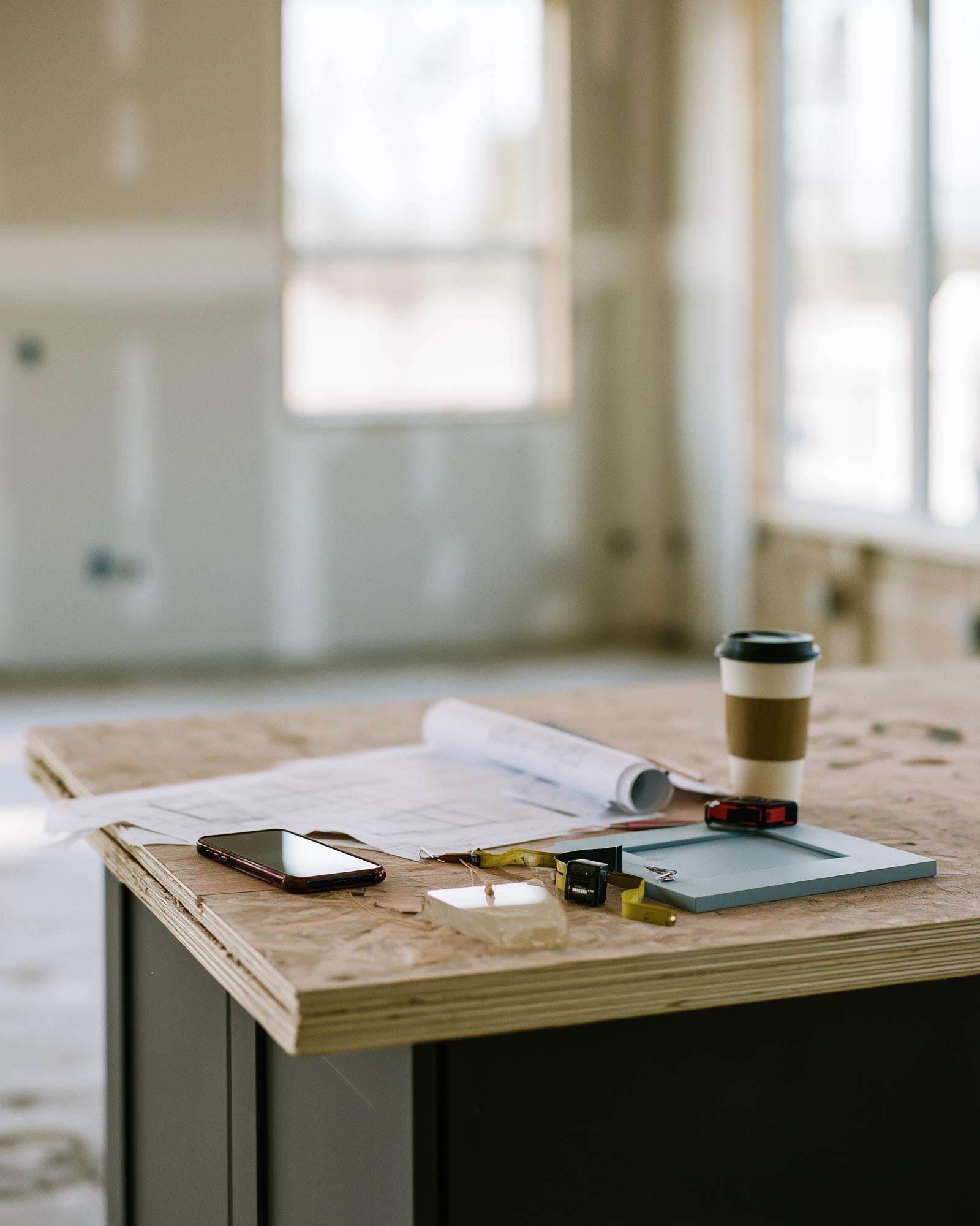 A phone, rolled plans, tape, and a door sample on a work surface